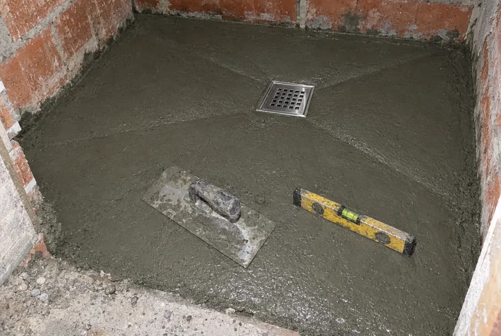 Mortero fresco con pendiente hacia un sumidero cuadrado de acero, con una llana y un nivel apoyados encima