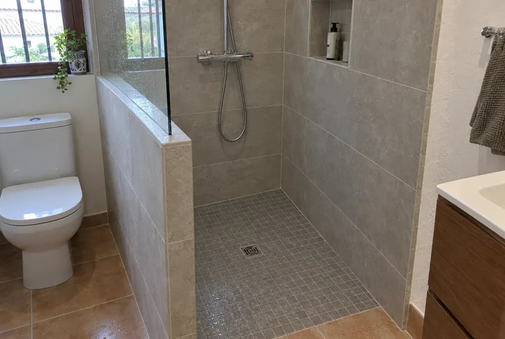 Plato de ducha de obra alicatado con mosaico gris antideslizante, sumidero cuadrado y murete de obra con cristal fijo