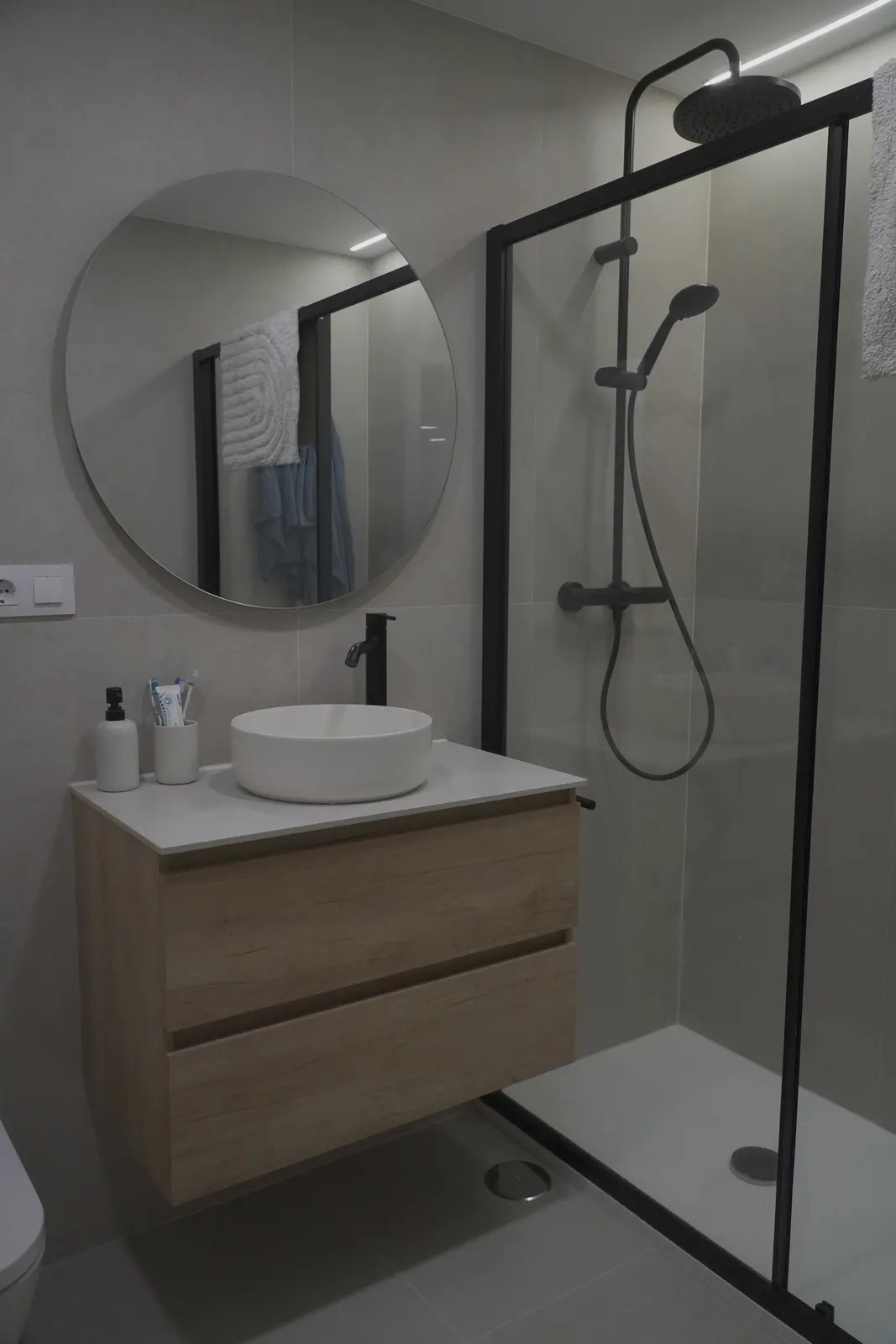 Mueble de baño suspendido de madera con lavabo sobre encimera y ducha de perfil negro